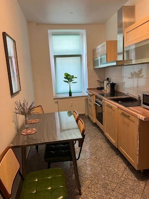 A compact kitchen with a dining table, chairs, and a window with a plant. - Leipzig Alt Lindenau Apartment – Sleeps 5, Parking (Leipzig)