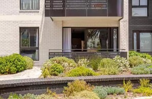 A modern two-story building with a balcony, surrounded by a landscaped garden with various shrubs and plants. - KML Nine Palms Luxury 101 (Cape Town)