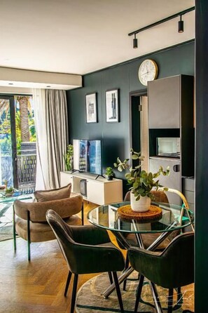 A modern living room with a glass dining table, black and brown chairs, a large mirror, and a television. - KML Nine Palms Luxury 101 (Cape Town)