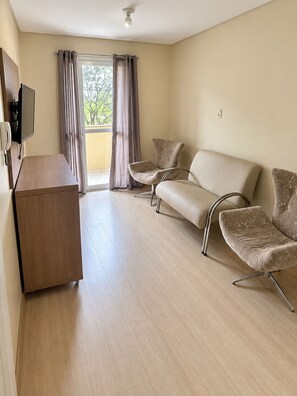 Een hotelkamer met een houten bureau, twee banken en een groot raam met gordijnen.