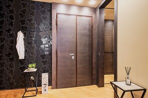 Ein Zimmer mit Holzboden, einer dunkel gemusterten Wand, einer doppelten Tür, einem kleinen Tisch mit Pflanze und einer Vase mit Ästen.