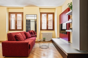 Ein Wohnzimmer mit einem roten Sofa, einem Glastisch und einem Fernseher auf einer weißen Kommode.