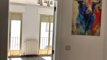 An interior hallway with a door leading to a balcony, a radiator, and a colorful bull painting on the wall.