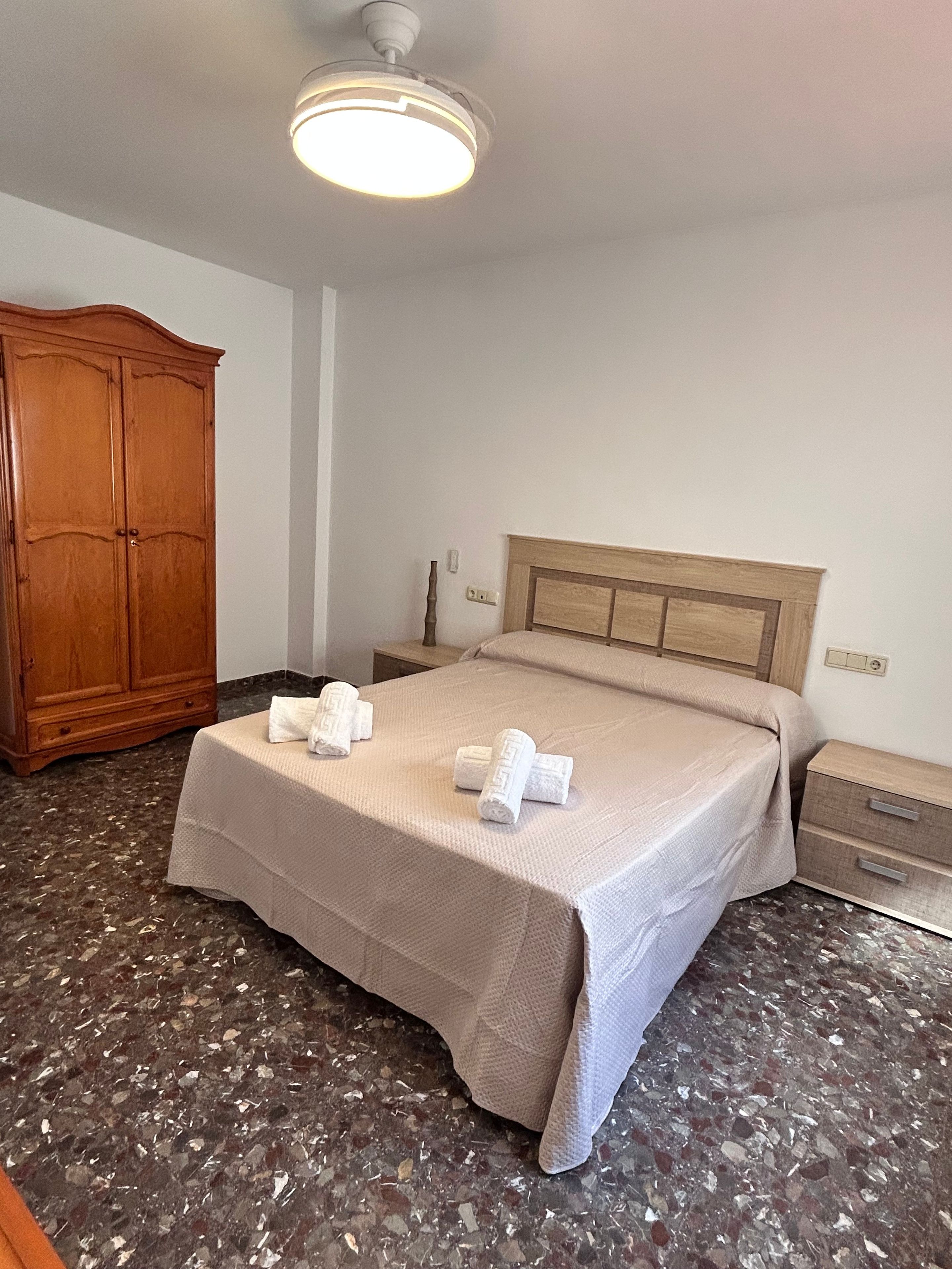 Una habitación de hotel con una cama, un armario de madera, una mesita de noche y una lámpara en el techo.