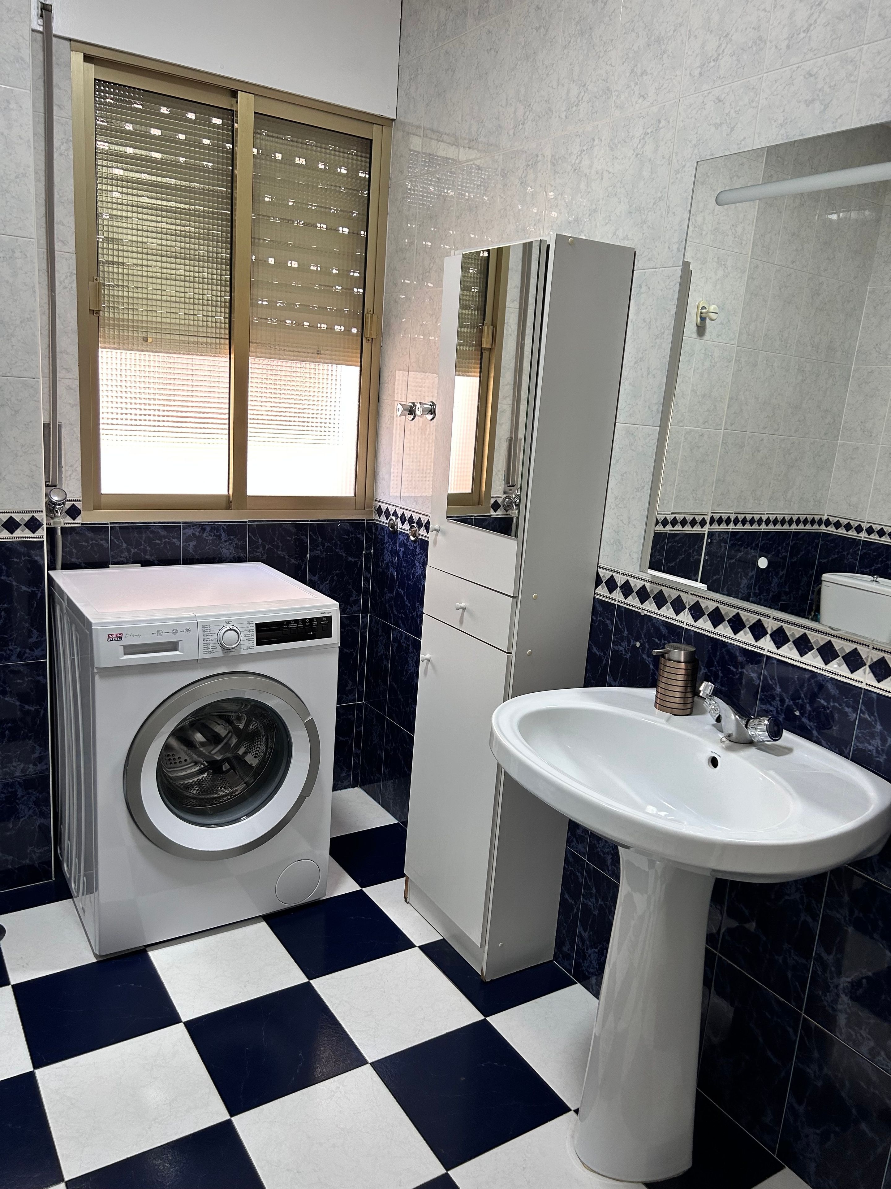 Un baño con lavadora, lavabo y ventana con persianas.