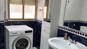 Un baño con lavadora, lavabo y ventana con persianas.