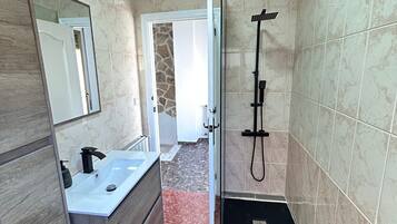 Un baño con tocador, ducha y puerta que da a otra habitación.