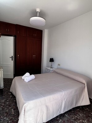 Una habitación de hotel con cama, mesita de noche, lámpara, armario y puerta.
