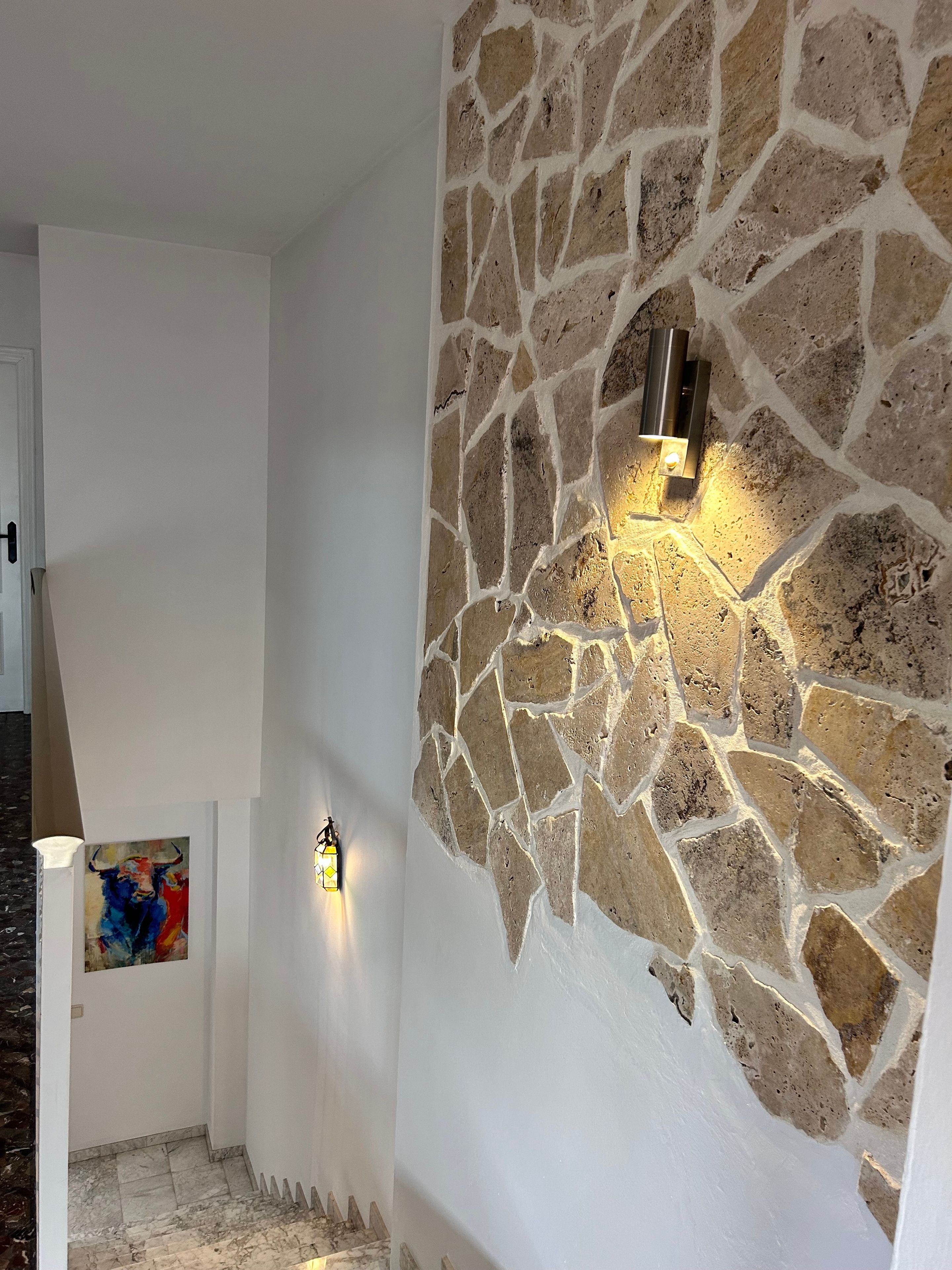 Un couloir avec un mur en pierre, une porte et un tableau.
