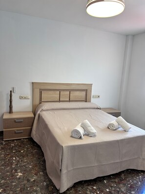 Una habitación de hotel con cama, mesita de noche, lámpara y toma de corriente.