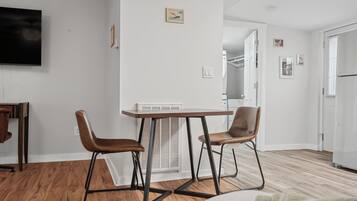 Un soggiorno moderno con pavimento in legno, un tavolo da pranzo con due sedie, una TV a schermo piatto montata a parete e una piccola foto incorniciata sopra il tavolo.