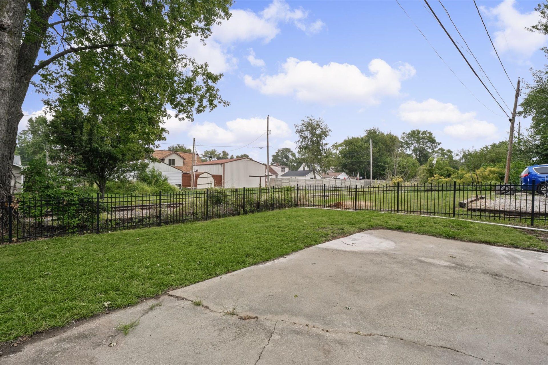 A residential area with a paved driveway, a fenced yard, and a building with a red roof.