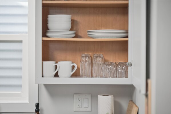 Un armario de cocina con platos, tazones y tazas blancos.