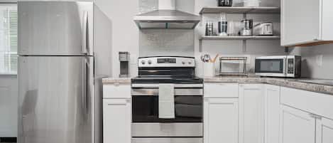 A modern kitchen with stainless steel appliances, white cabinetry, and a wood floor.
