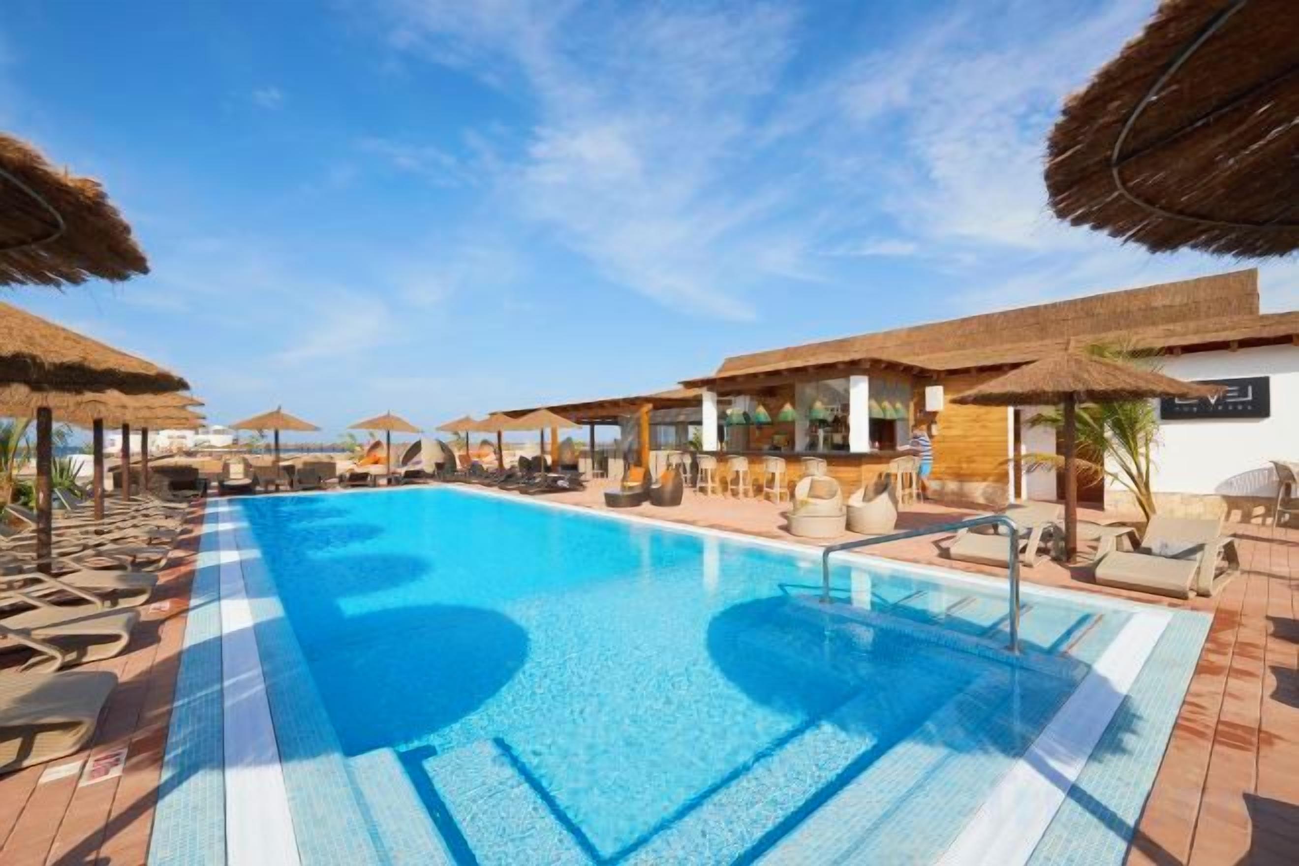 Piscina com espreguiçadeiras e guarda-sóis, cercada por uma área coberta com vista para o mar.