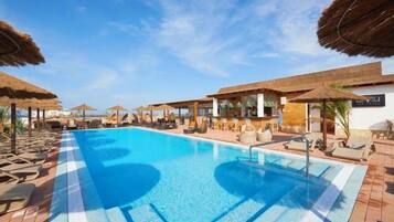 Piscina com espreguiçadeiras e guarda-sóis, cercada por uma área coberta com vista para o mar.