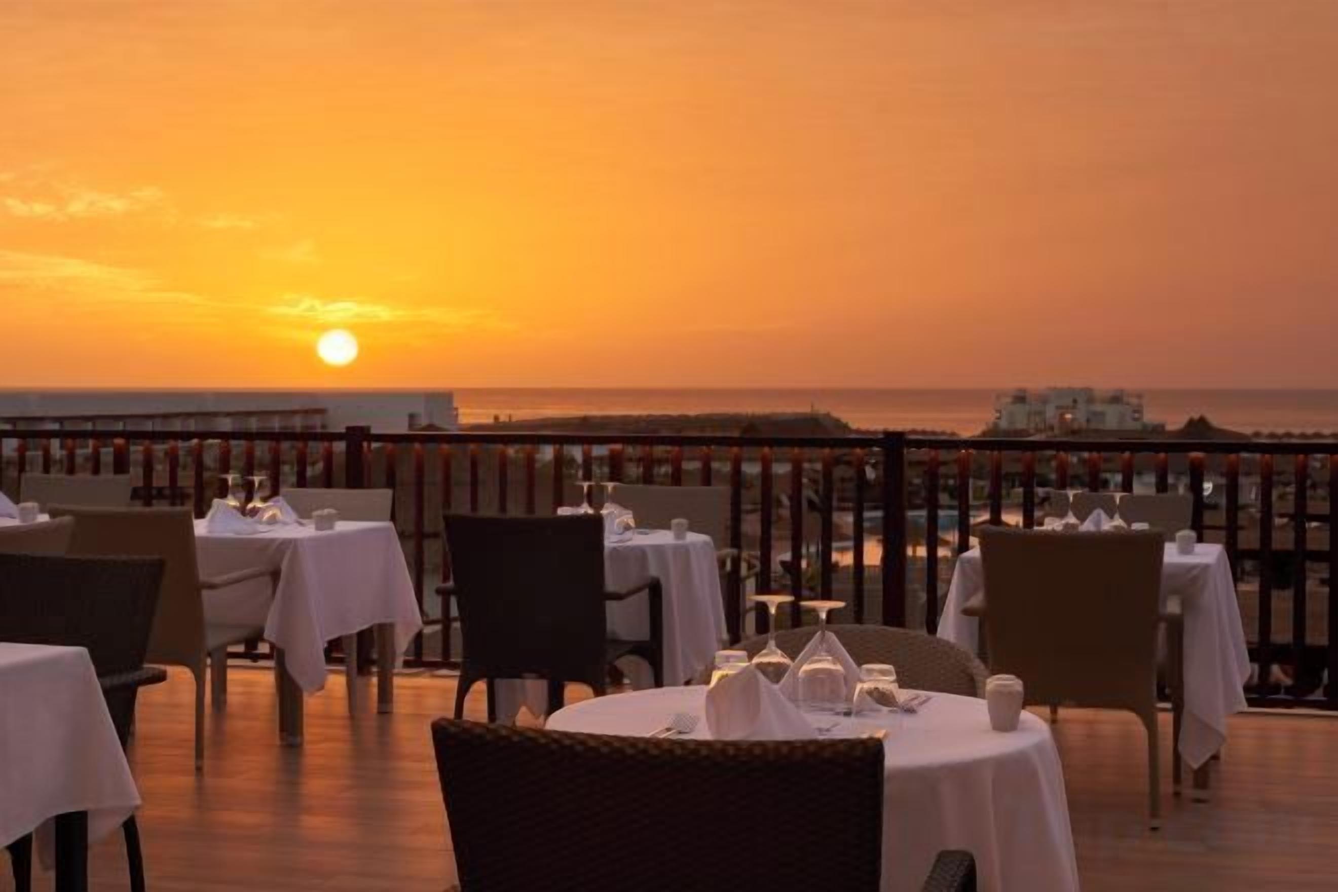 Una terraza con mesas dispuestas para comer, con vista a la puesta de sol y al mar.