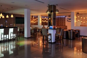 Um hall de hotel moderno com área de bar, sofás e luminárias decorativas.