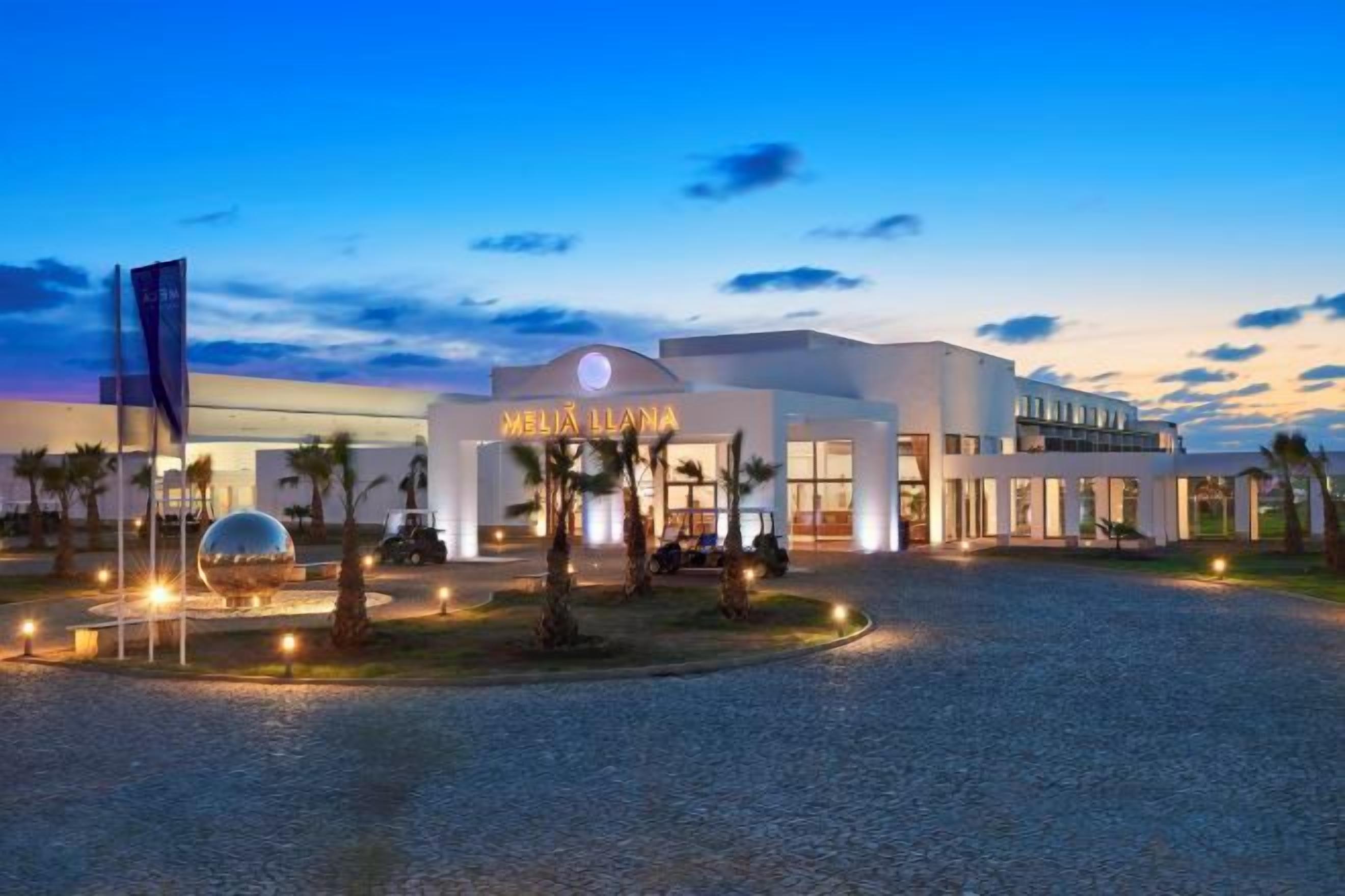 Hotel com design moderno, entrada bem iluminada e acesso por calçada pavimentada.