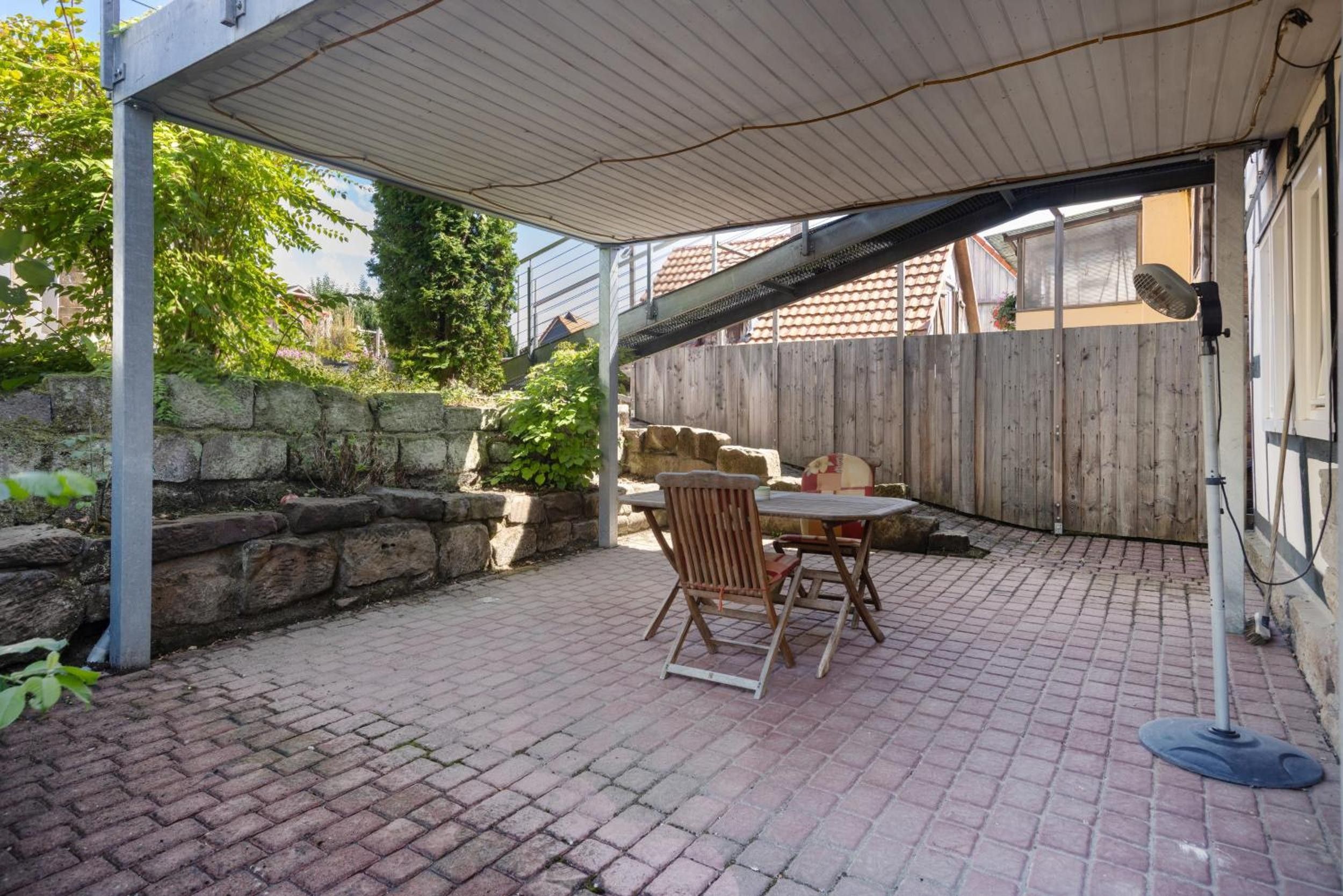 Ein überdachter Patio-Bereich mit Terrazzo, einem Tisch und zwei Stühlen.