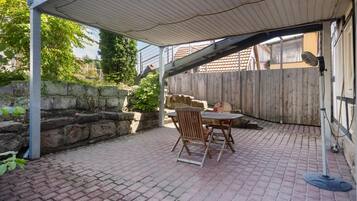 A covered patio area with a brick floor, a table, and two chairs.