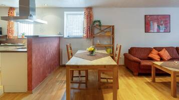 A cozy living room with a wooden dining table, a sofa, and a kitchen area with a stove and cabinets.