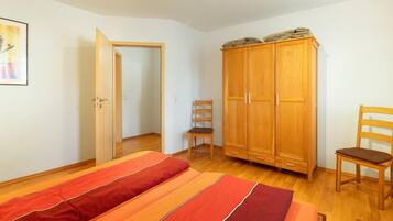 A bedroom with a bed, two chairs, a wardrobe, and a door leading to another room.