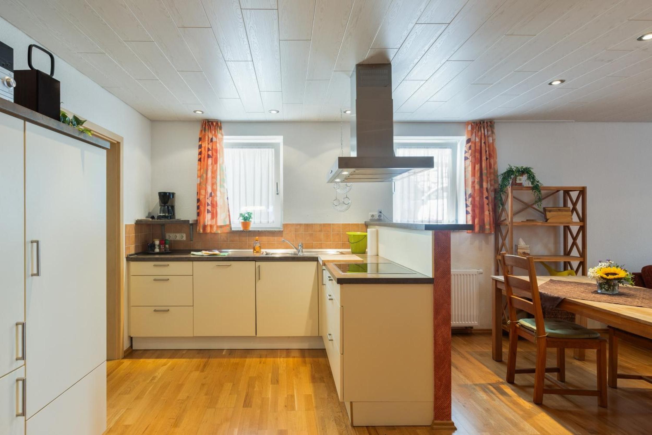 Cocina compacta con suelo de madera, estufa integrada, lavaplatos y comedor con mesa y sillas.