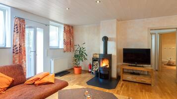 A cozy living room with a sofa, a television, a fireplace, and a potted plant.