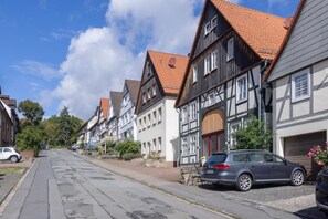 A street lined with traditional half-timbered houses, a parked car, and a clear blue sky.