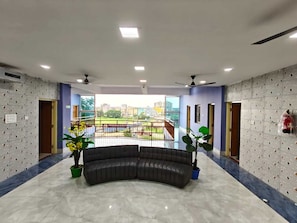 A hotel lobby with a curved black leather sofa, potted plants, a balcony with a railing, and a cityscape view. - Hotel O Atala Main Road (Balianta)