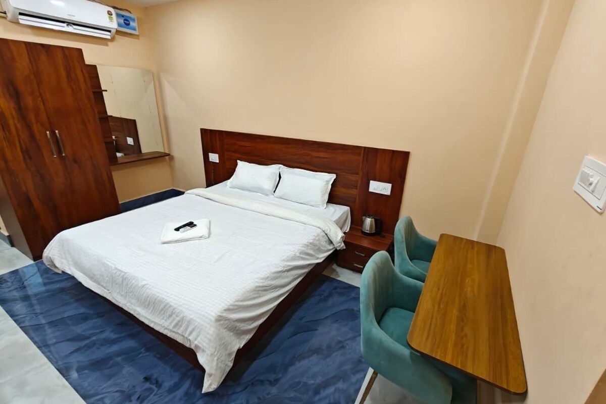 A hotel room with a bed, a desk, a chair, and an air conditioning unit.