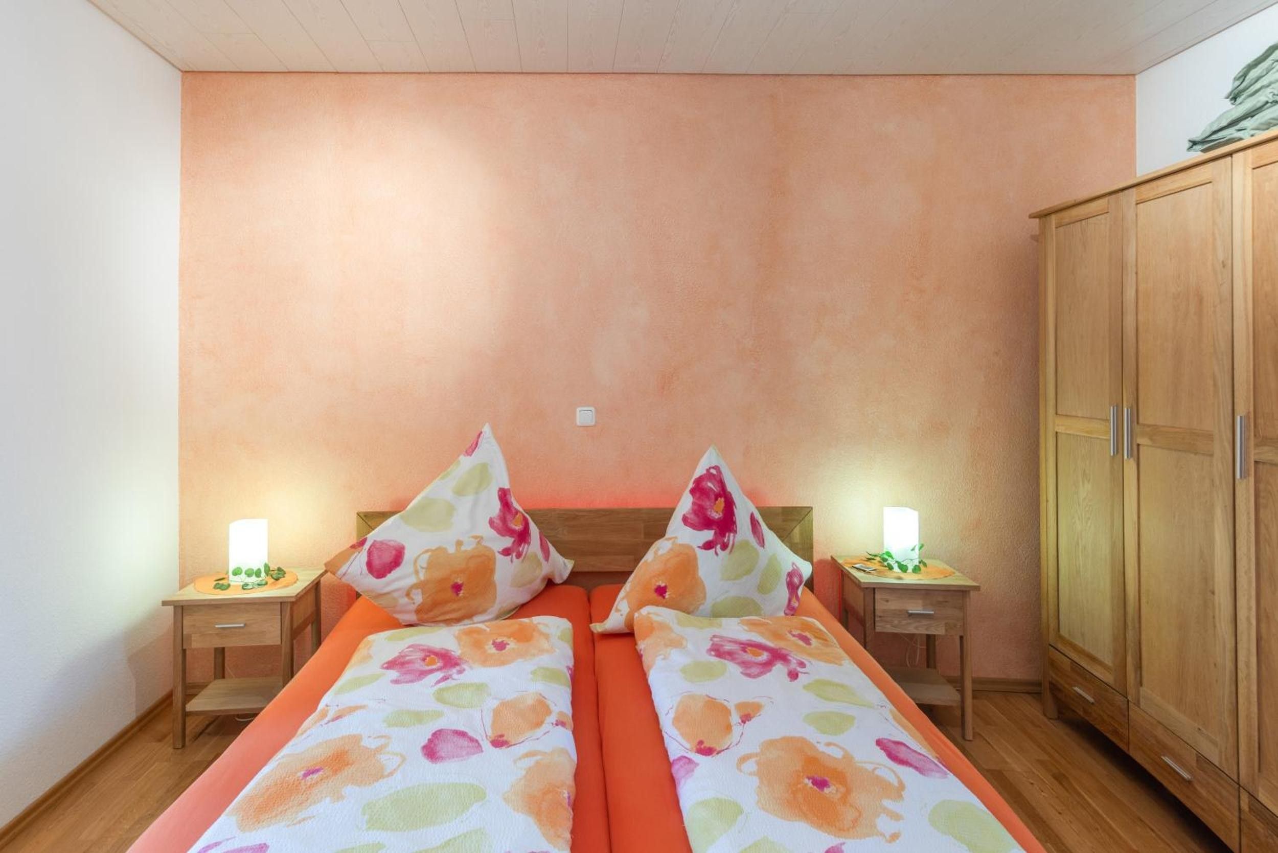 A double bed with floral bedding, two bedside tables with lamps, and a wardrobe.