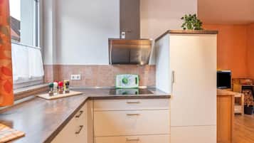 Cocina compacta con extractor de aire empotrado, ventana con cortinas y una pequeña planta en maceta sobre la encimera.