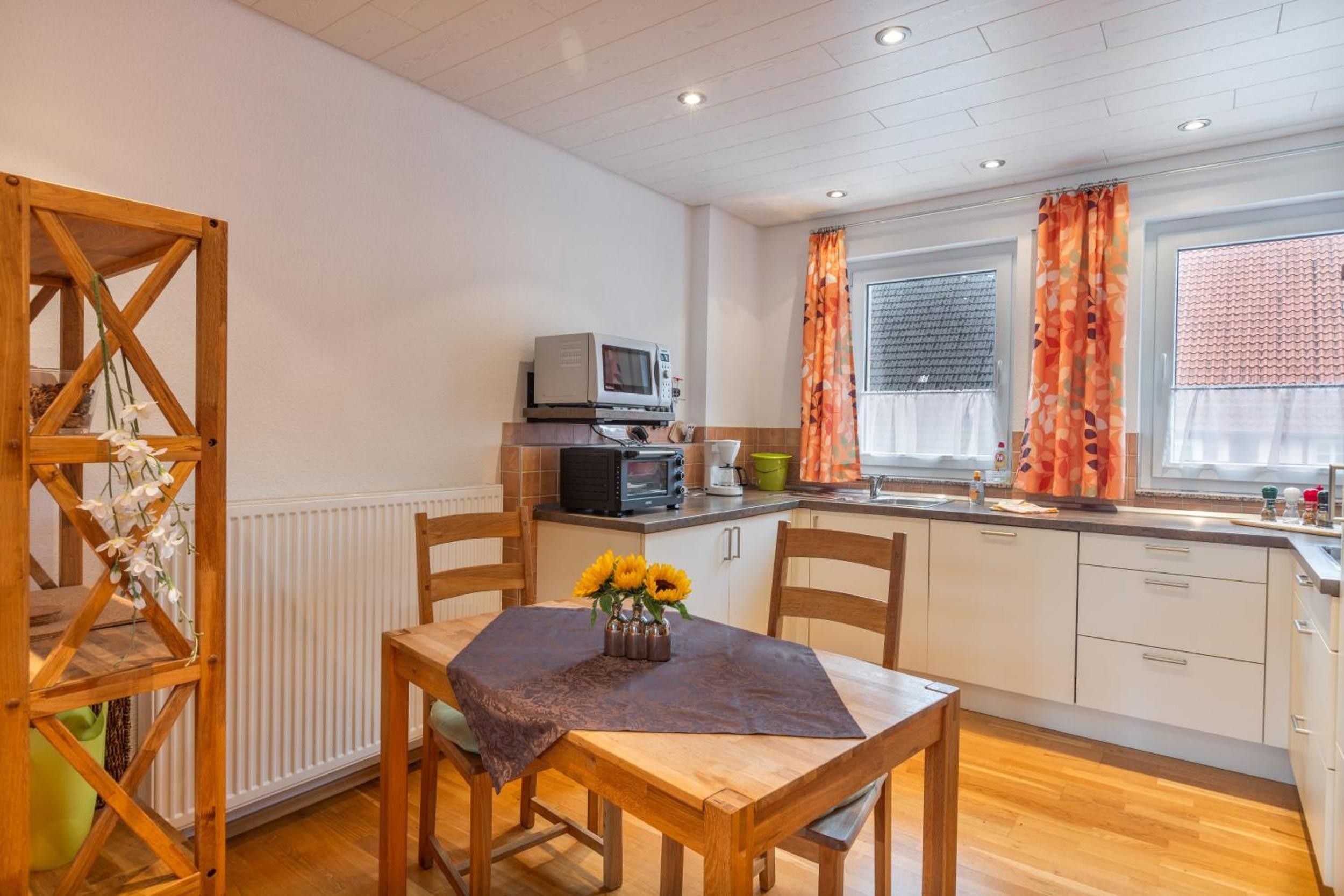 A compact kitchen with a dining area, featuring a wooden table with a vase of sunflowers, a microwave, and a kettle.