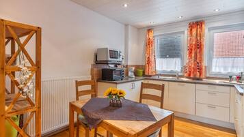 A compact kitchen with a dining area, featuring a wooden table with a vase of sunflowers, a microwave, and a kettle.