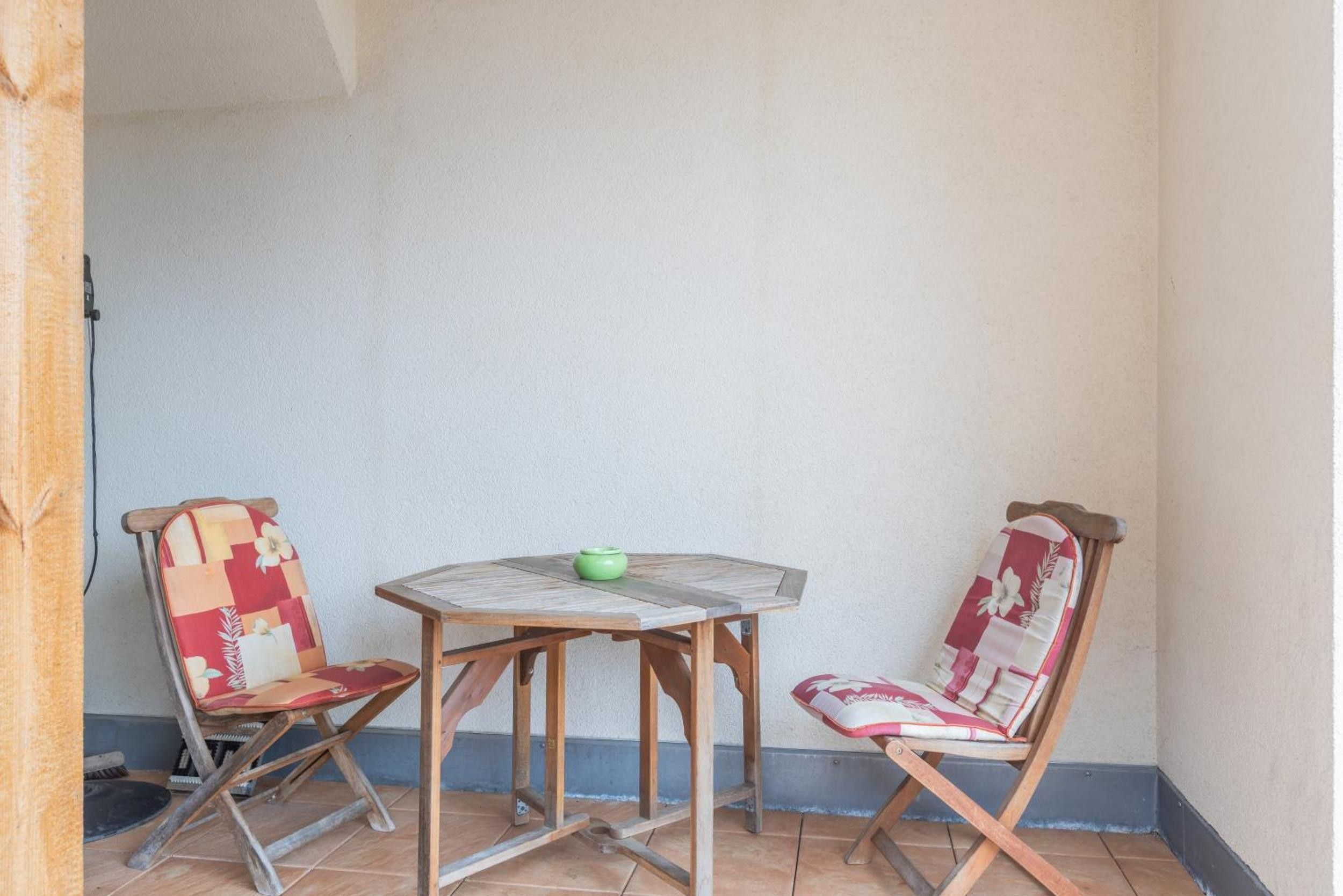 Un pequeño patio con una mesa redonda de madera y dos sillas con tapicería floral.