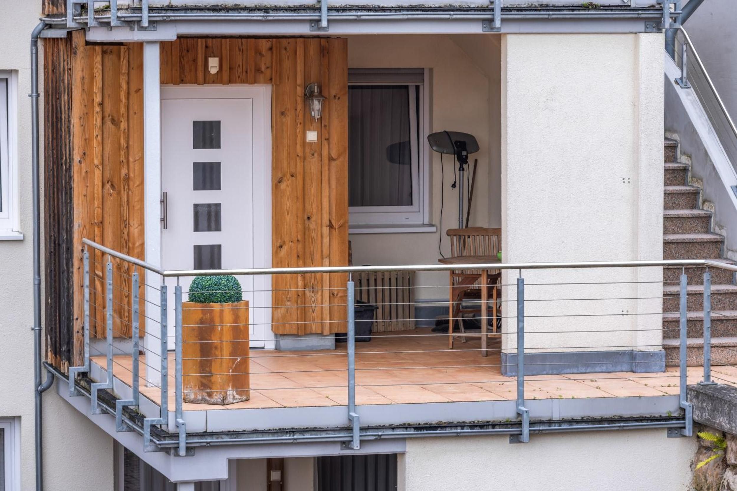 A residential building with a wooden exterior, a balcony with a metal railing, a door, and a window.