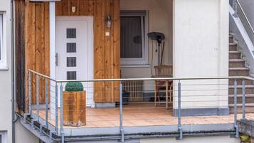 A residential building with a wooden exterior, a balcony with a metal railing, a door, and a window.