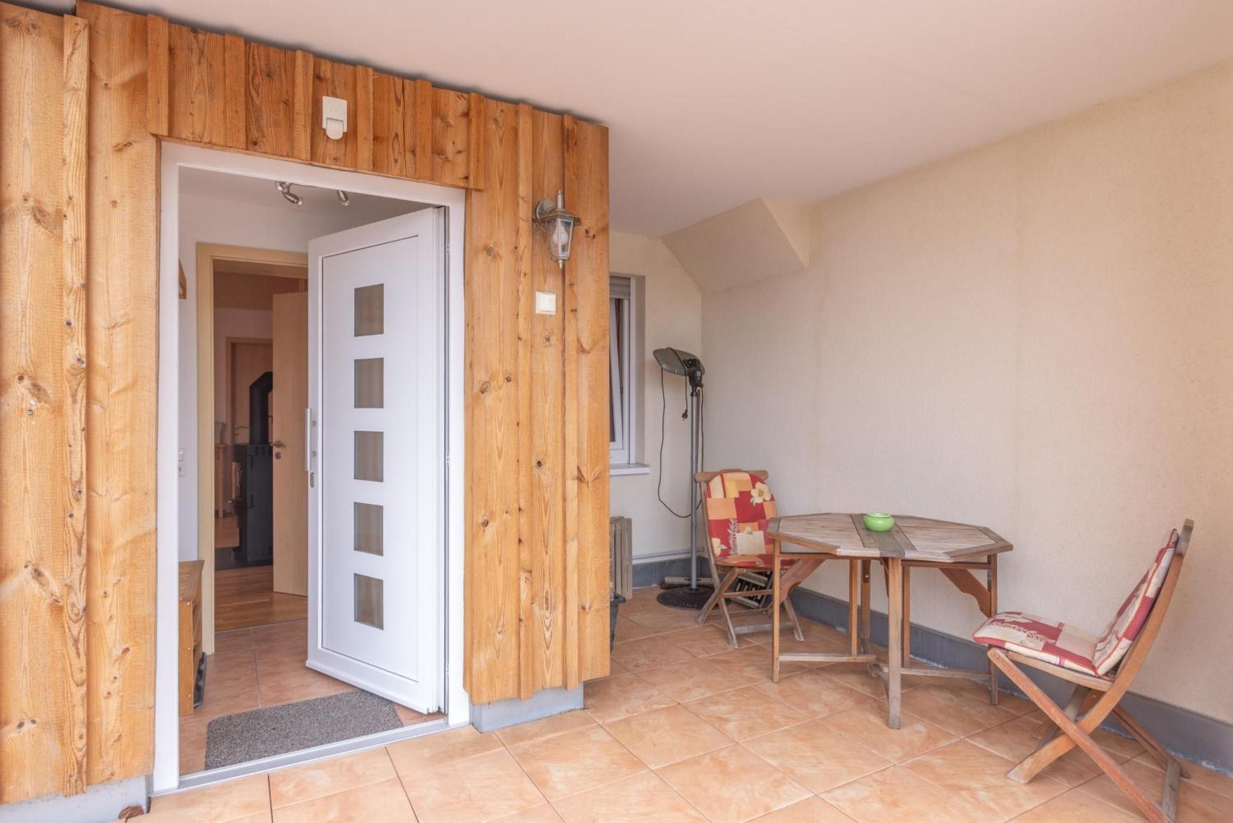 A room with a wooden door, a small table with a chair, and a floor lamp.