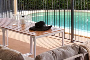 A wooden table with a hat and glasses, overlooking a pool. - Binnea Beach House & 1 Bedroom Garden Suite (Sunshine Coast)