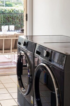 A front view of a modern, two-door front-loading washing machine in a residential setting. - Binnea Beach House & 1 Bedroom Garden Suite (Sunshine Coast)