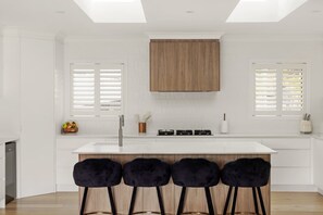 A modern kitchen with a central island, white cabinetry, and a skylight. - Binnea Beach House & 1 Bedroom Garden Suite (Sunshine Coast)