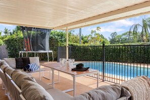 Un área de estar exterior con piscina, una mesa y un porche cubierto.