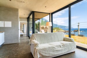 A modern living room with a sofa, a lamp, and a view of the sea. - A breathtaking view, peace, quiet, nature, and of course, great waves! (São Vicente)