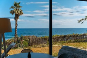 A room with a view of the ocean, a palm tree, and a table with a lamp. - A breathtaking view, peace, quiet, nature, and of course, great waves! (São Vicente)