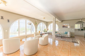 A spacious living area with a sofa, chairs, a coffee table, and a kitchen in the background. - Villa 'Casa Bergerac' with Sea View, Wi-Fi and Air Conditioning (Cómpeta)