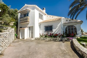 A two-story house with a stone wall, a balcony, and a garden with flowers. - Villa 'Casa Bergerac' with Sea View, Wi-Fi and Air Conditioning (Cómpeta)