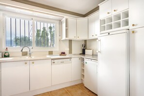 A kitchen with white cabinets, a built-in dishwasher, and a window with a view of trees. - Villa 'Casa Bergerac' with Sea View, Wi-Fi and Air Conditioning (Cómpeta)