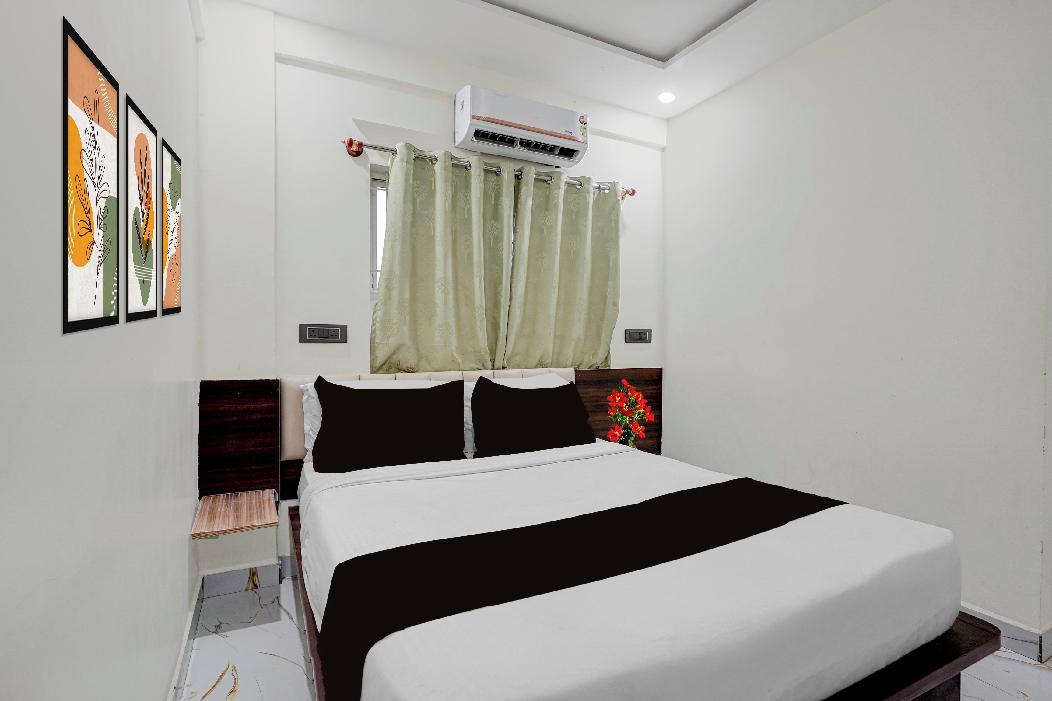A hotel room with a bed, a window with curtains, an air conditioning unit, and framed artwork on the wall.